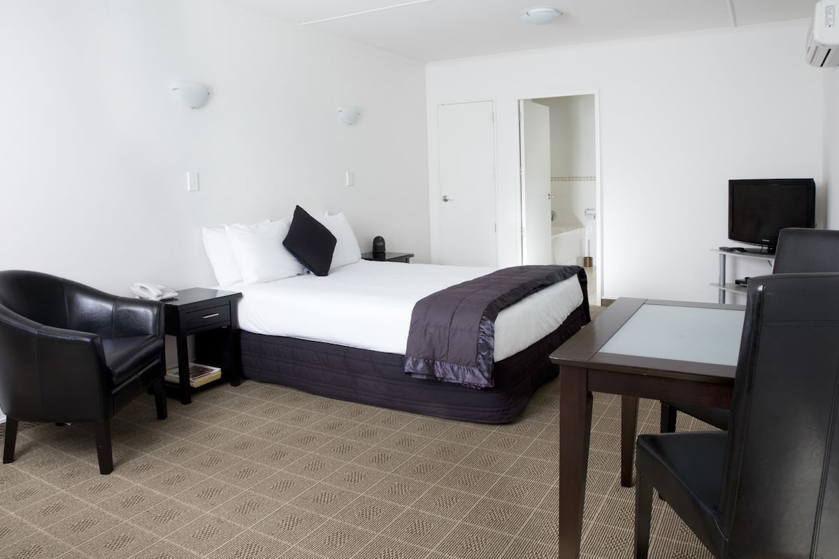 A hotel room with a bed, a desk, two chairs, a television, and a door leading to another room.