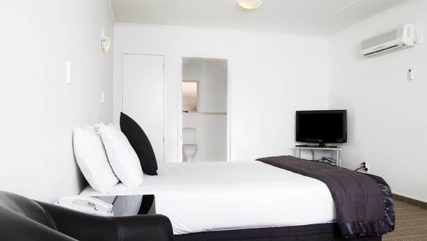 A hotel room with a bed, a television on a stand, a desk, and a chair. - Hygate Motor Lodge (Hamilton)