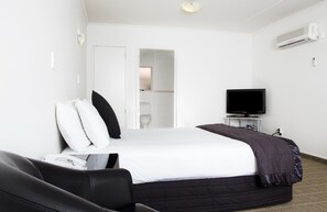 A hotel room with a bed, a television on a stand, a desk, and a chair. - Hygate Motor Lodge (Hamilton)