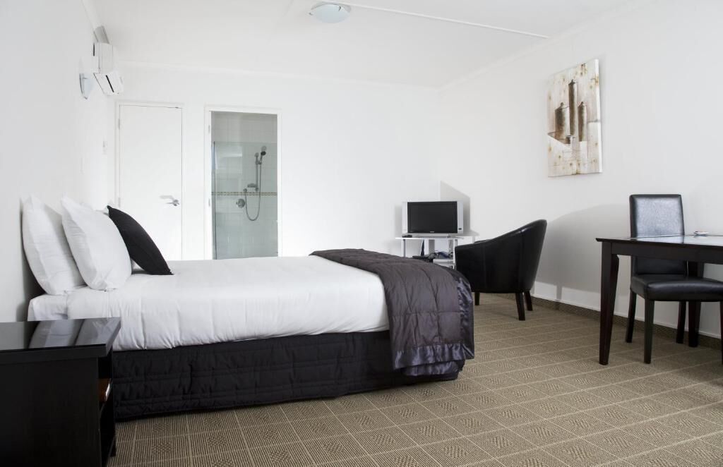 A hotel room with a bed, a desk with a computer, a chair, and a shower area.