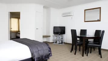 Una habitación de hotel con cama, televisor, mesa de comedor con sillas y un equipo de aire acondicionado en la pared.