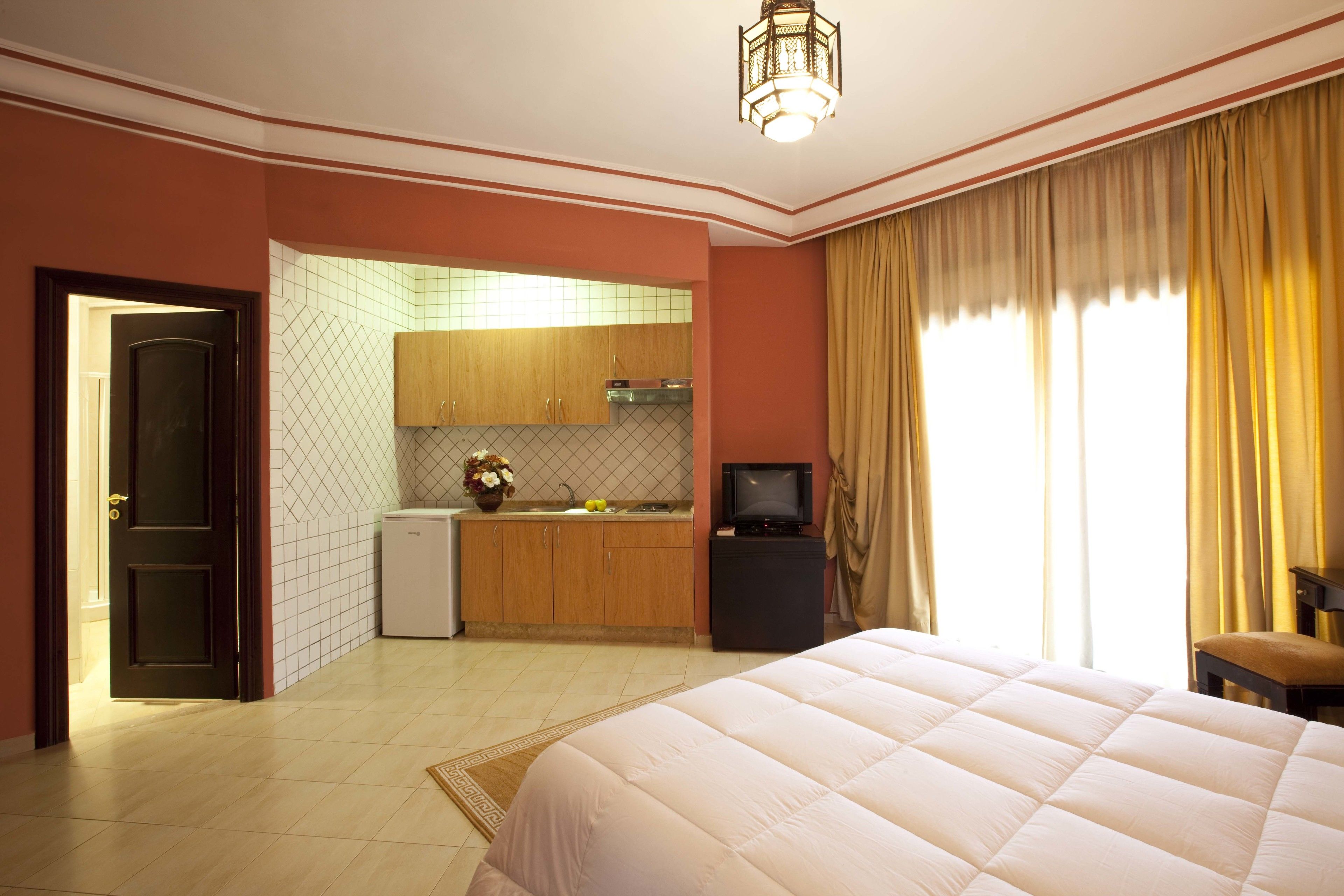 A hotel room with a bed, a television, a kitchenette, and a bathroom.