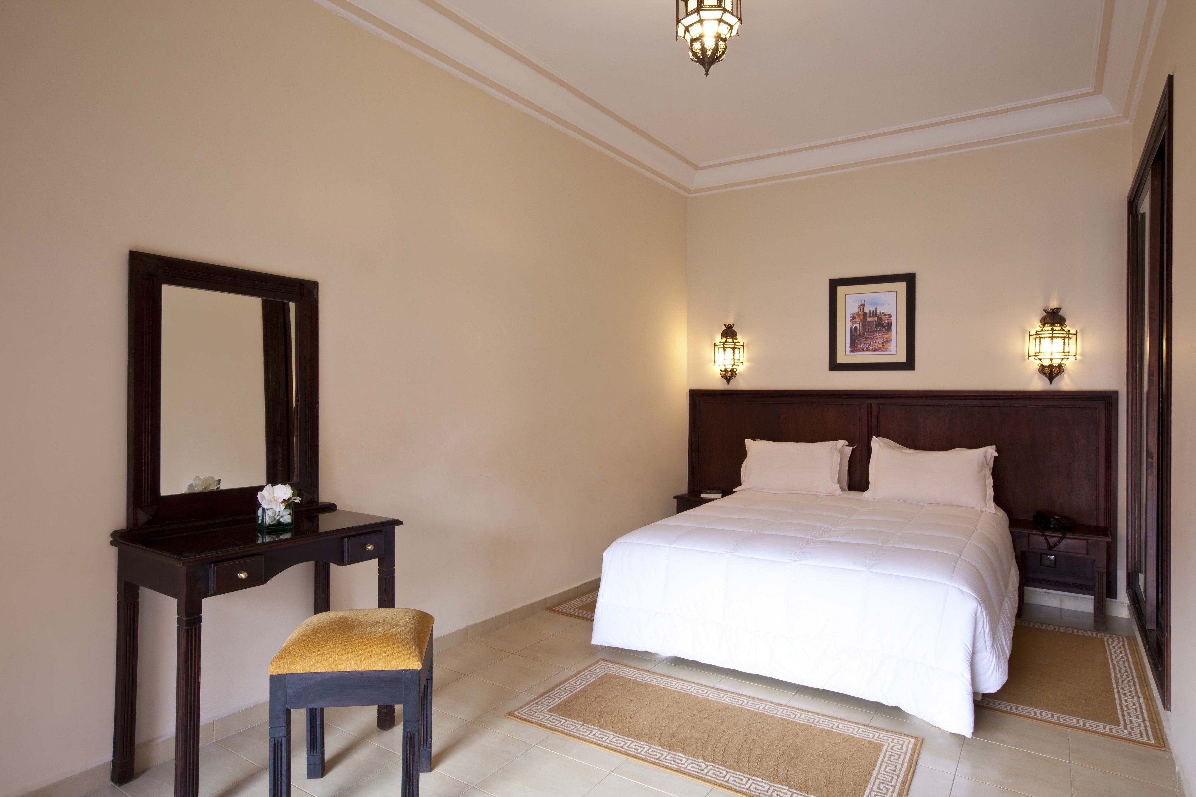 A hotel room with a large bed, a bedside table, a chair, a mirror, and two wall-mounted lamps.
