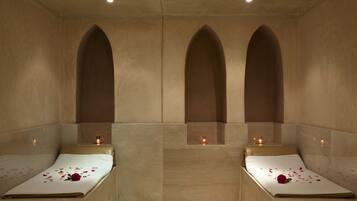 Ein Spa-Zimmer mit zwei Betten, auf jedem Bett eine Rose und auf den Nachttischen Kerzen.