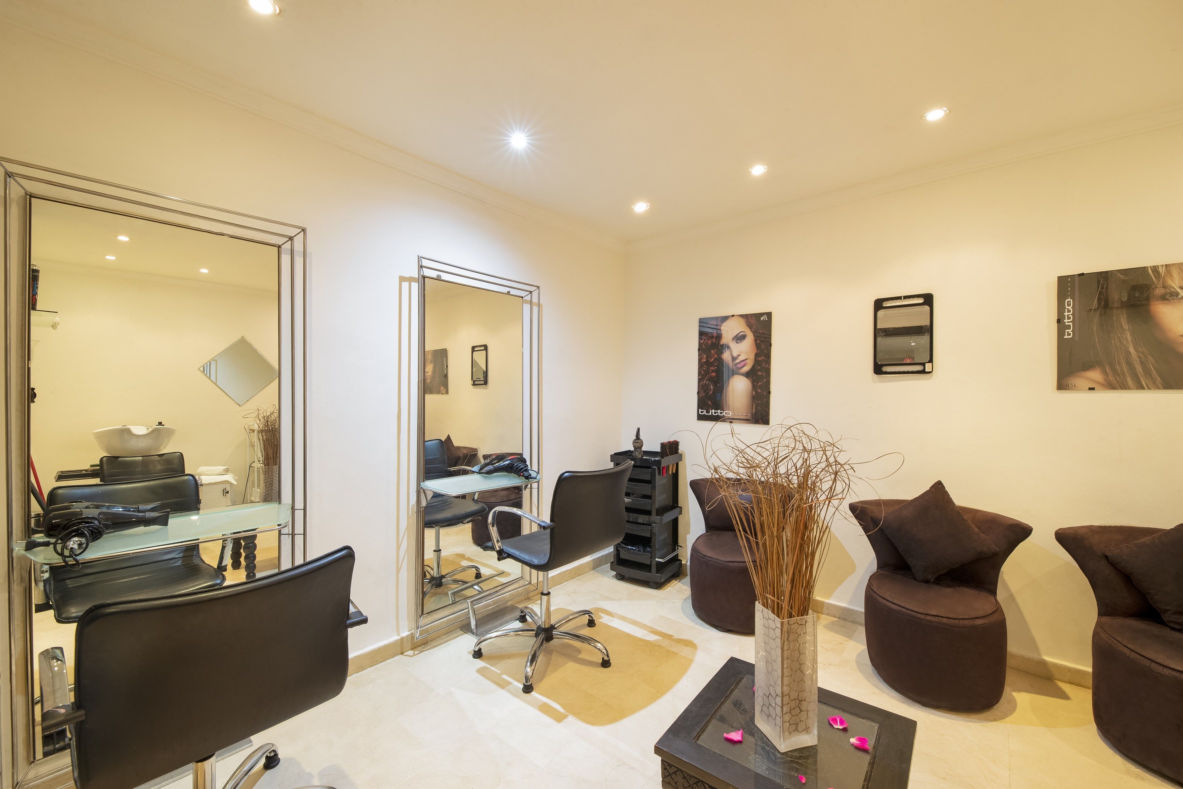 A modern salon with a large mirror, black salon chairs, a glass table, and a vase with dried plants.