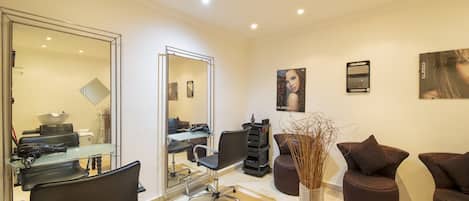 Een moderne kapsalon met een grote spiegel, zwarte kappersstoelen, een glazen tafel en een vaas met gedroogde planten.