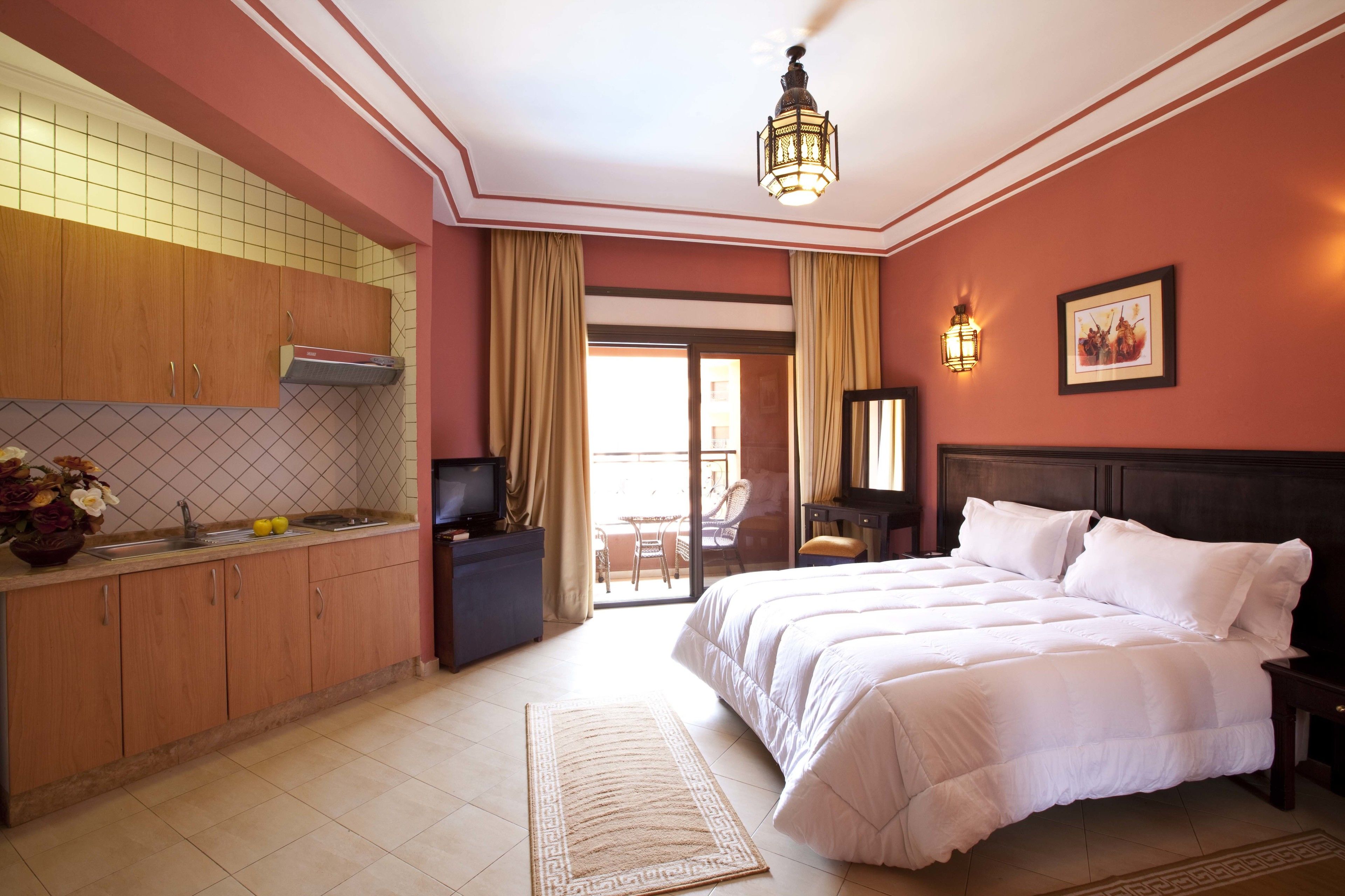 Une chambre d’hôtel dotée d’un grand lit, d’une kitchenette, d’un coin repas avec une table et des chaises, et d’une porte-fenêtre coulissante donnant sur l’extérieur.