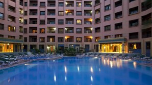 A hotel with a large indoor pool surrounded by lounge chairs and a multi-story building with balconies. - Mogador MENZAH (Marrakech)