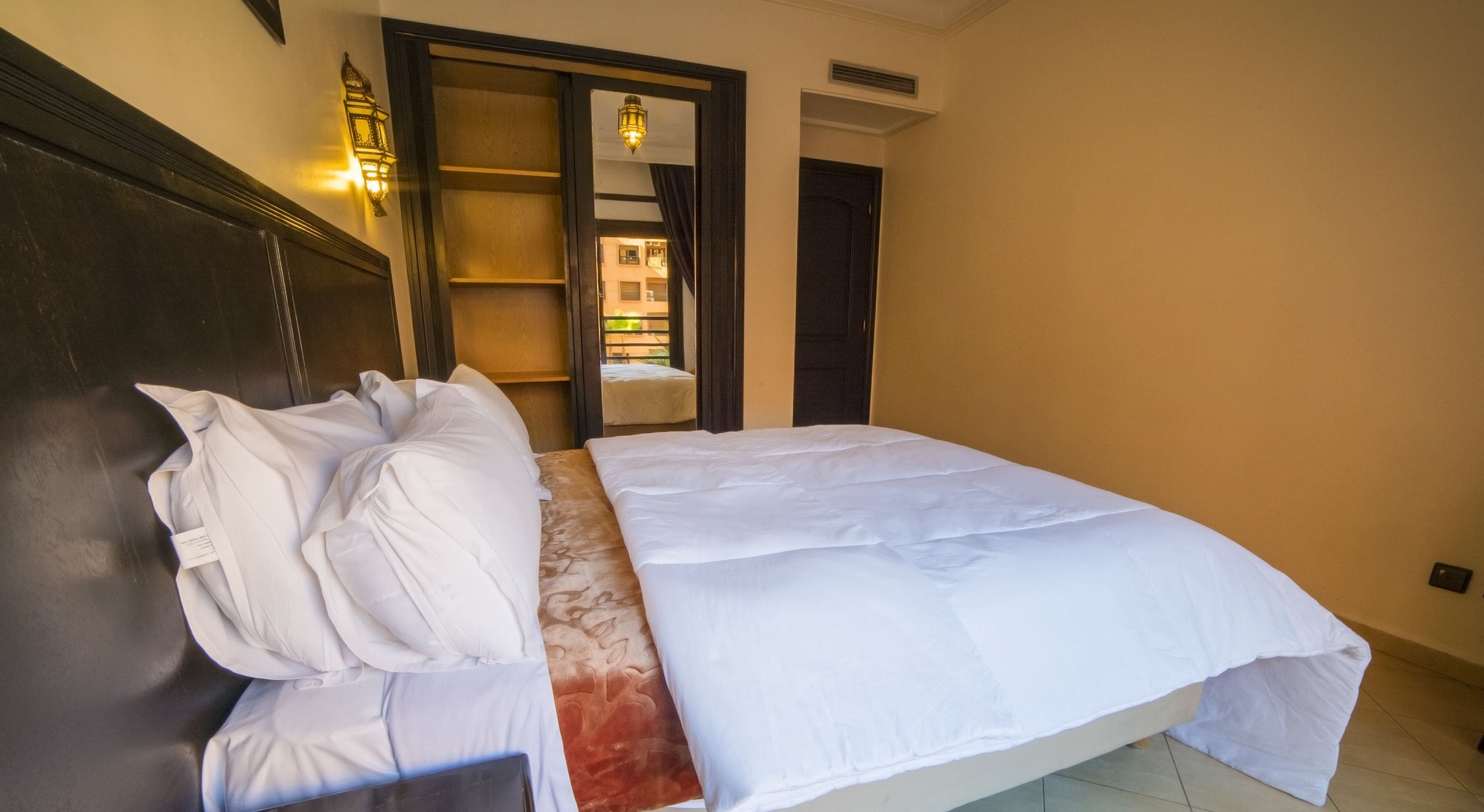 A neatly made bed with white linens, a dark wooden headboard, and a patterned runner.