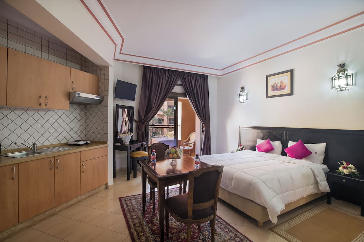 A compact hotel room with a kitchenette, a dining area, and a bed with a headboard.