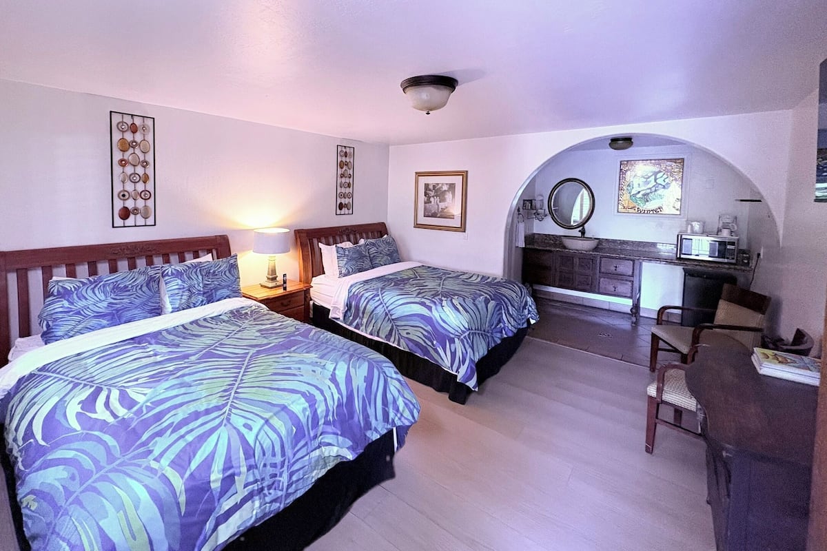 A bedroom with two beds, a desk, a chair, and a vanity with a mirror.