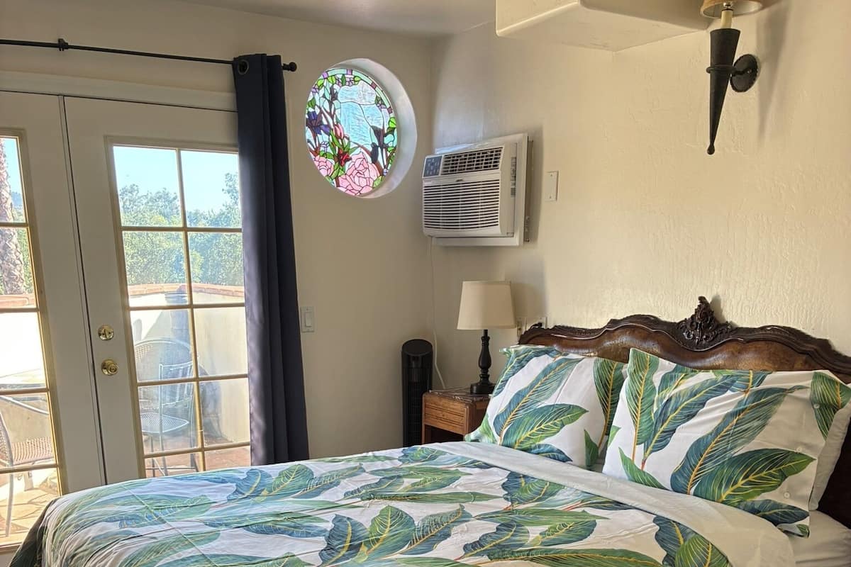 A bedroom with a bed, a window, a wall-mounted air conditioner, and a circular stained glass window.