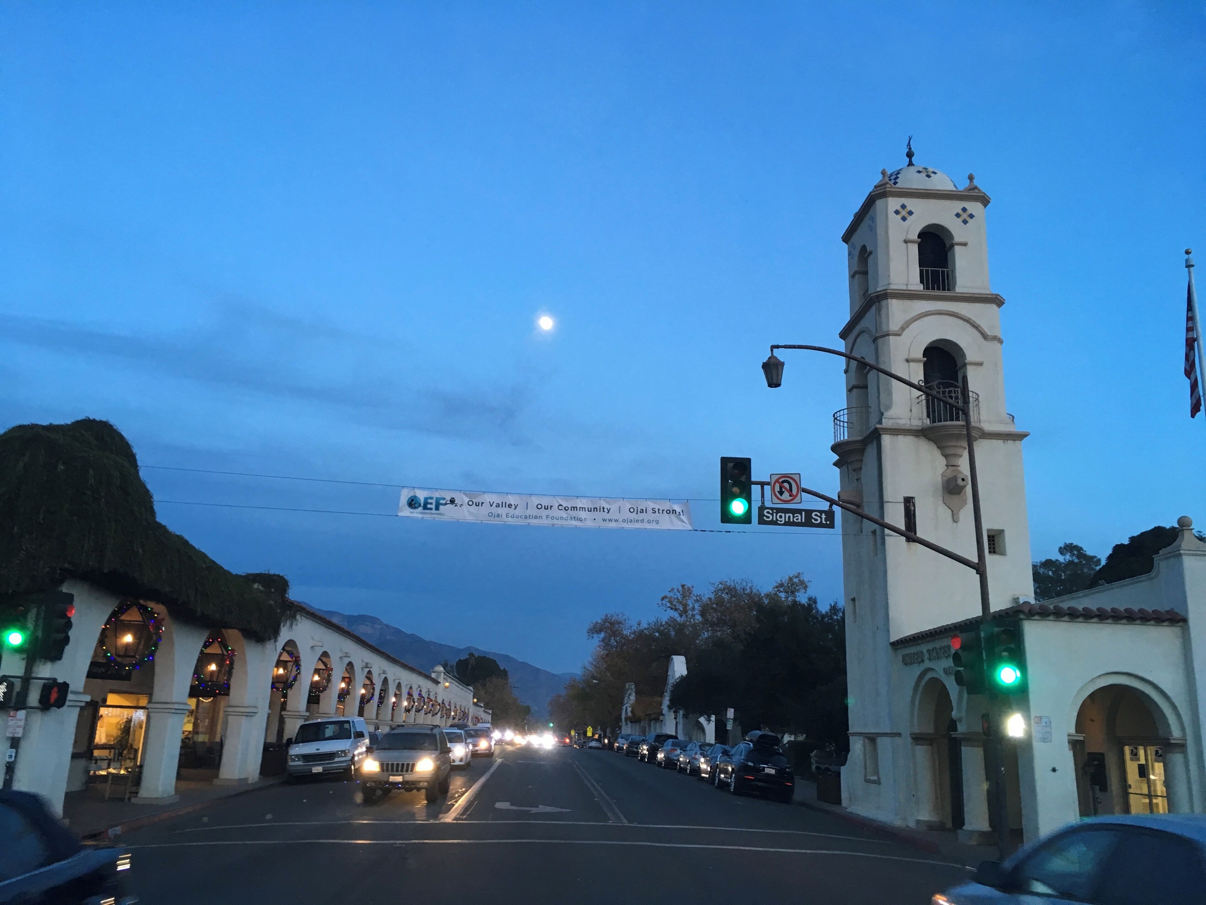 Una calle con un edificio blanco que cuenta con una torre de campanas, un banderín e indicación de tráfico.