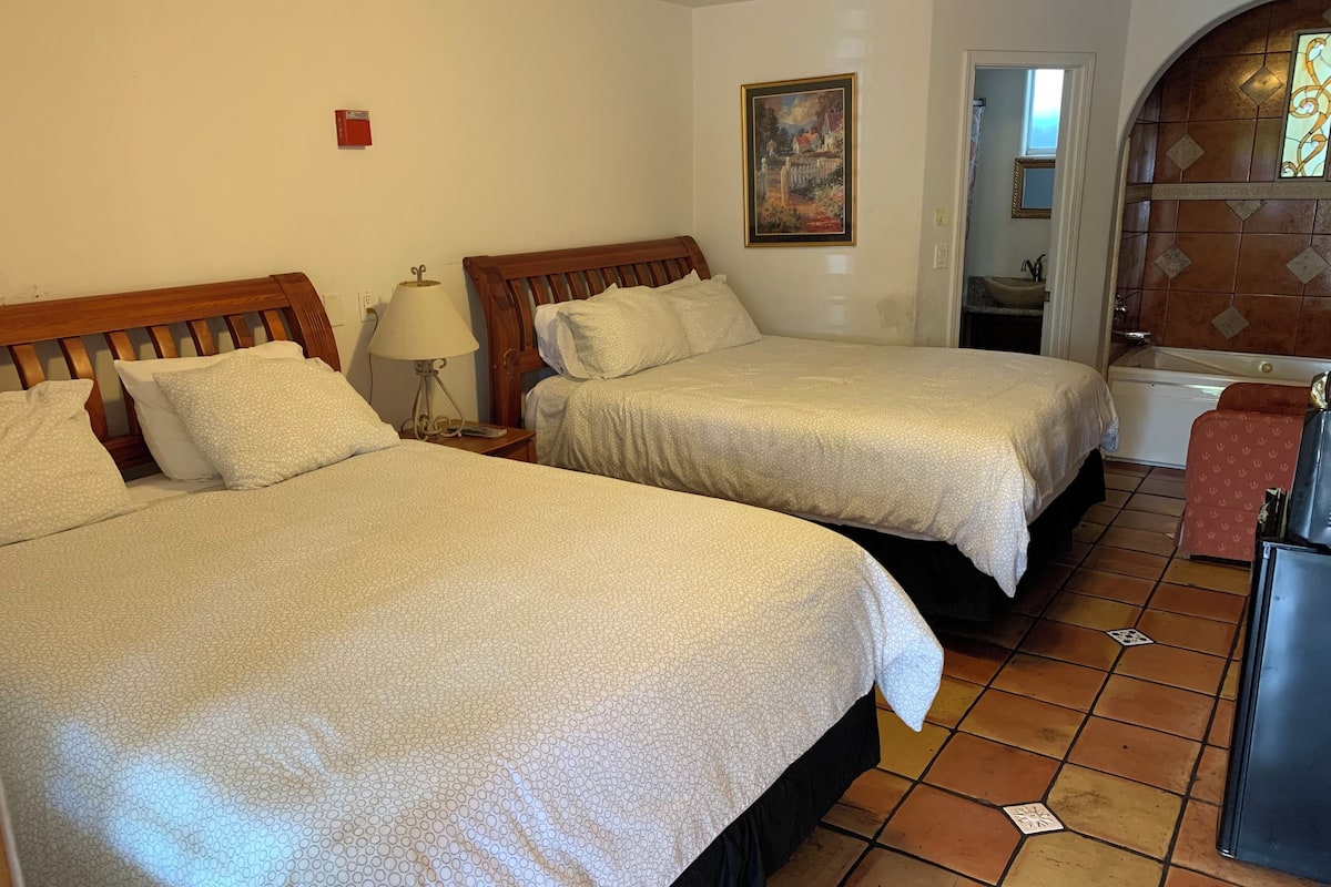 A hotel room with two beds, a bathroom with a bathtub, and a tiled floor.