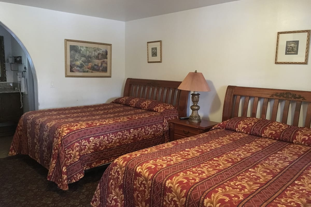 A room with two beds, a lamp, and framed pictures on the walls.