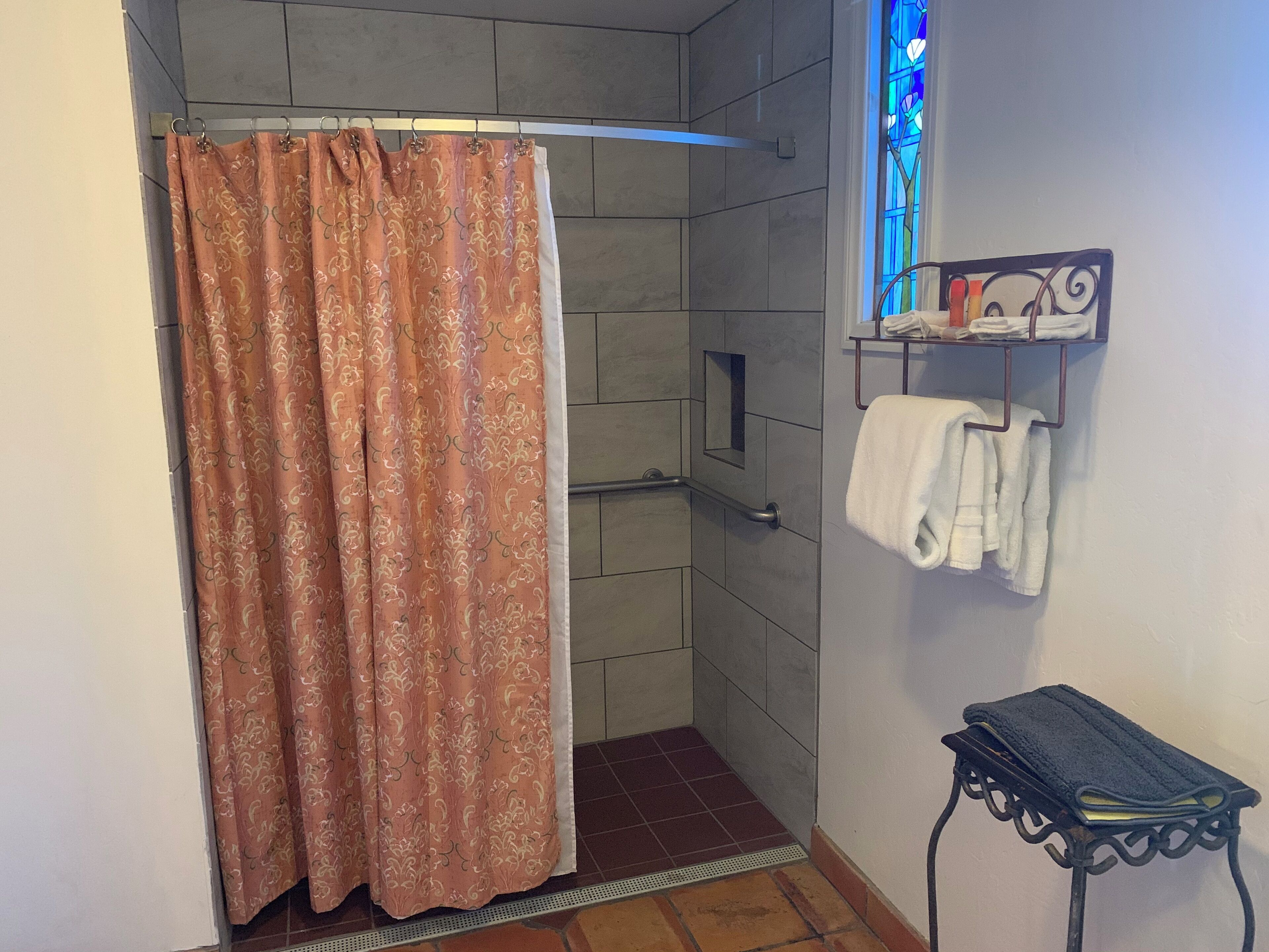 A bathroom with a shower curtain, a towel rack with towels, and a small table with a towel.