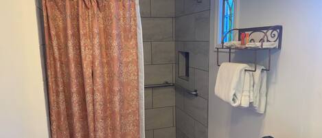 A bathroom with a shower curtain, a towel rack with towels, and a small table with a towel.