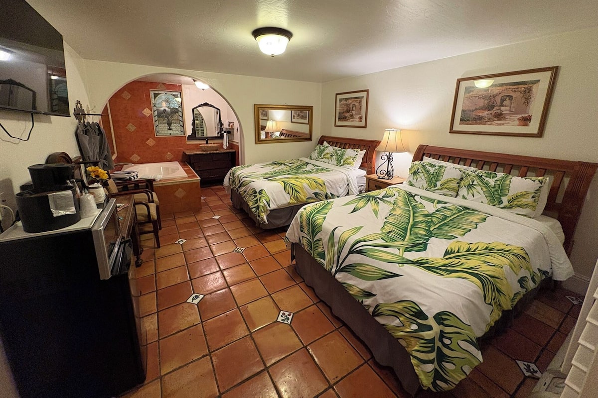A hotel room with two beds, a desk, a vanity, and a bathroom.
