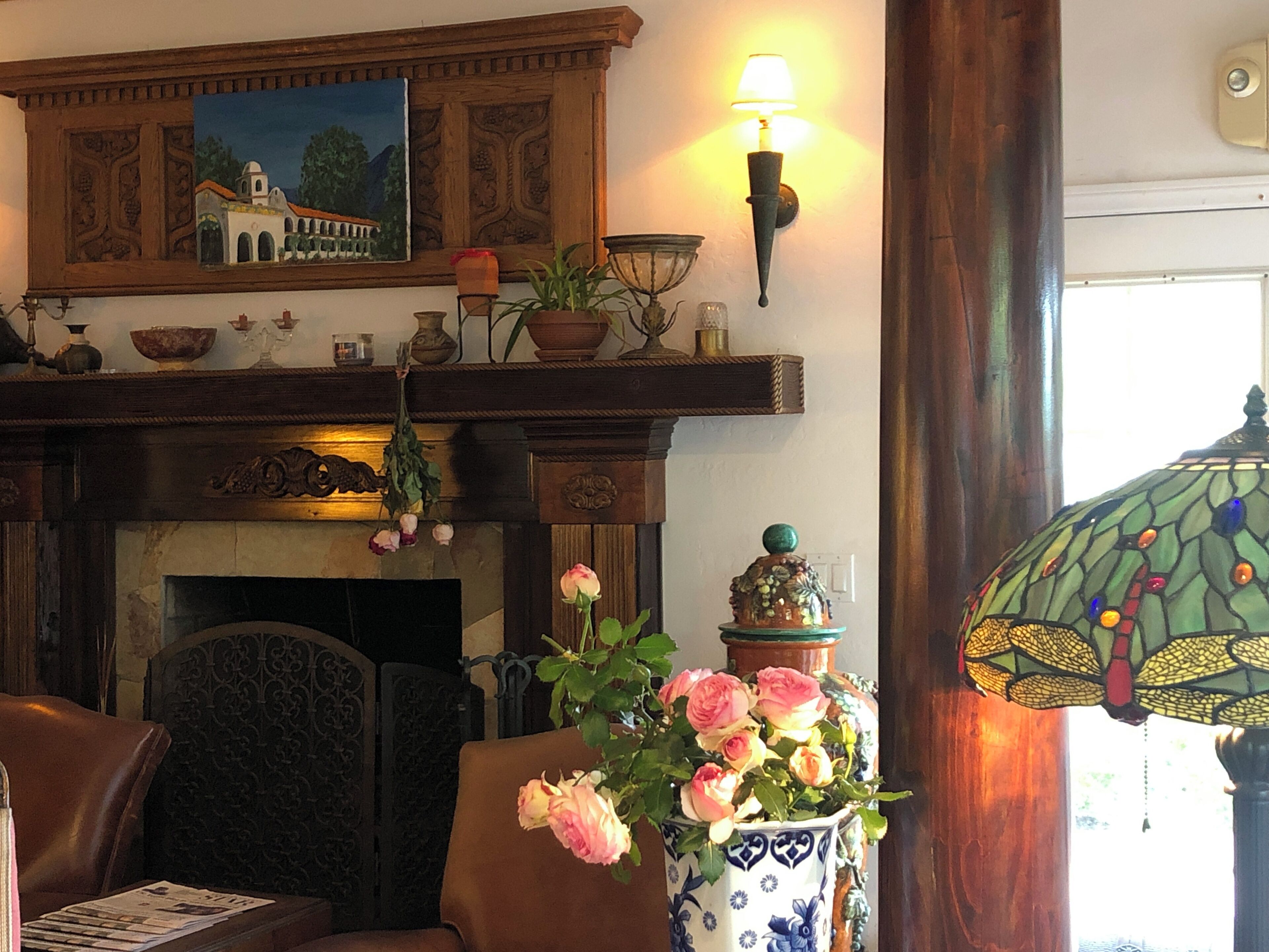 A cozy living room with a fireplace, a painting above it, and a vase with flowers on a table.