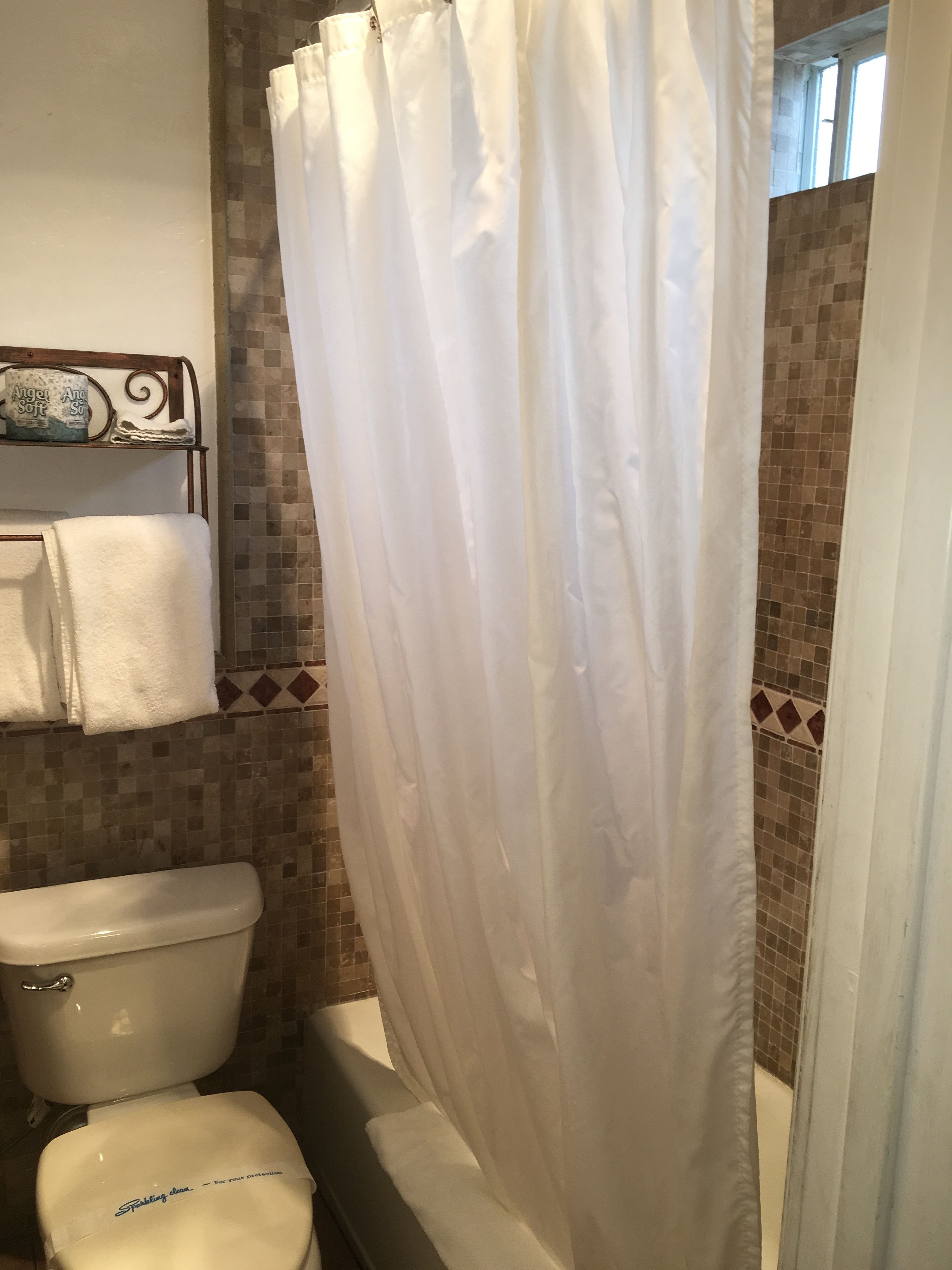 A bathroom with a shower curtain, a toilet, and a shelf with towels and a bottle of Angel Soft.