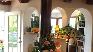 A room with a wooden table, a vase with flowers, a bowl of fruit, and a stained glass lamp.