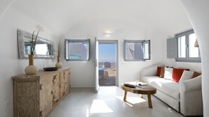 A spacious living area with a white sofa, a wooden cabinet, and a view through an open door to the outside.