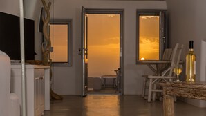A modern interior with a kitchen, dining area, and a view of the sunset through an arched doorway.