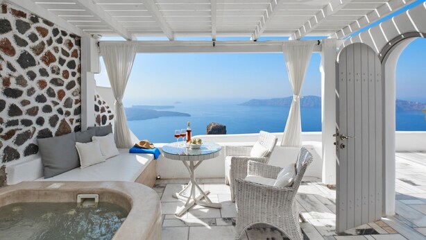 A terrace with a stone wall, a hot tub, wicker furniture, and a view of the sea.