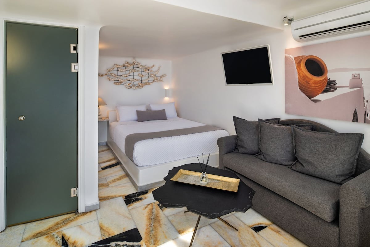 A bedroom with a bed, a gray sofa, a black coffee table, and a wall-mounted TV.