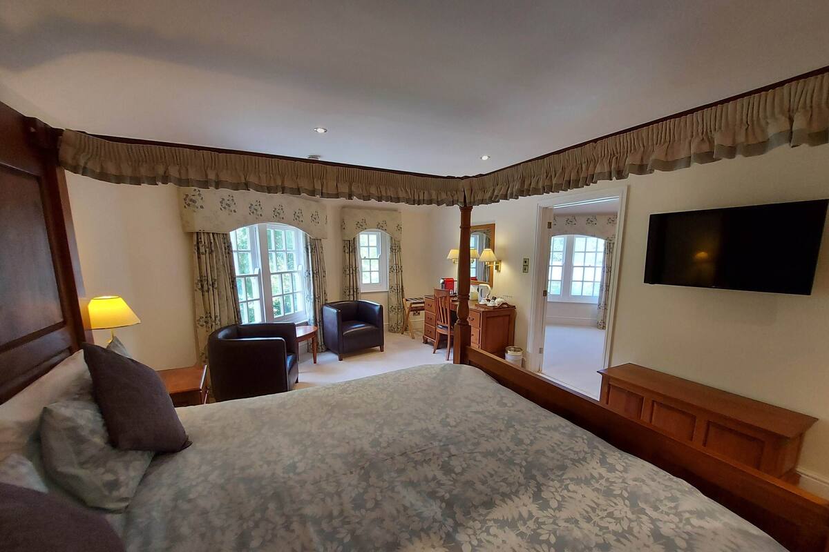 A bedroom with a large bed, two armchairs, a desk, a television, and a mirror.