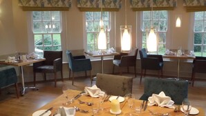 A dining area with tables set for four, chairs, and hanging pendant lights.