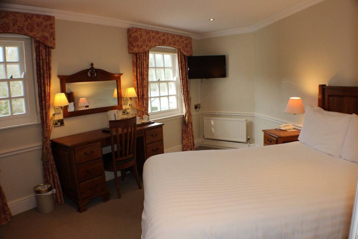 A hotel room with a bed, a desk with a chair, a television, and a radiator.