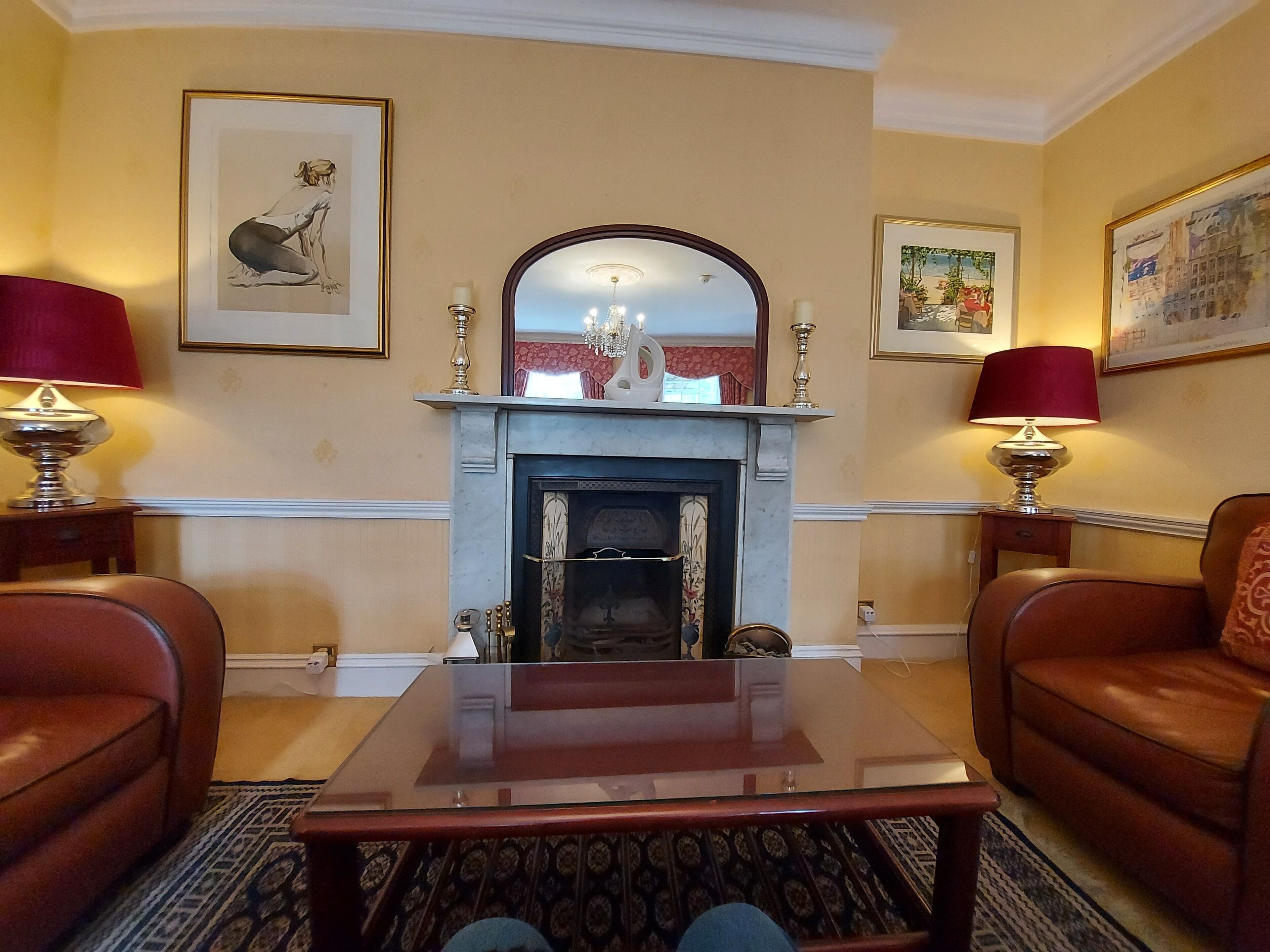 A room with a fireplace, two leather armchairs, a glass coffee table, and two lamps on side tables.