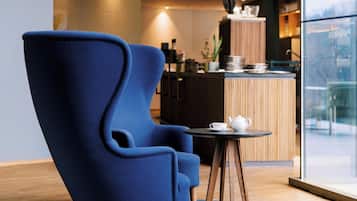 A modern room with a blue armchair, a small round table with a teapot, and a view of the city through large windows.