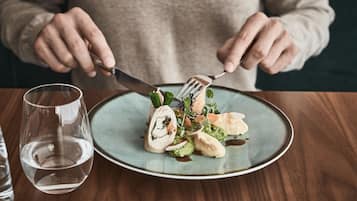 A person holding a fork and knife over a plate of food with a glass of water on the table.