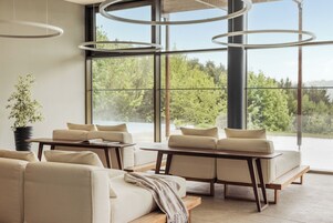 Una sala de estar moderna con un sofá, una mesa de centro y vistas a un bosque a través de amplios ventanales.