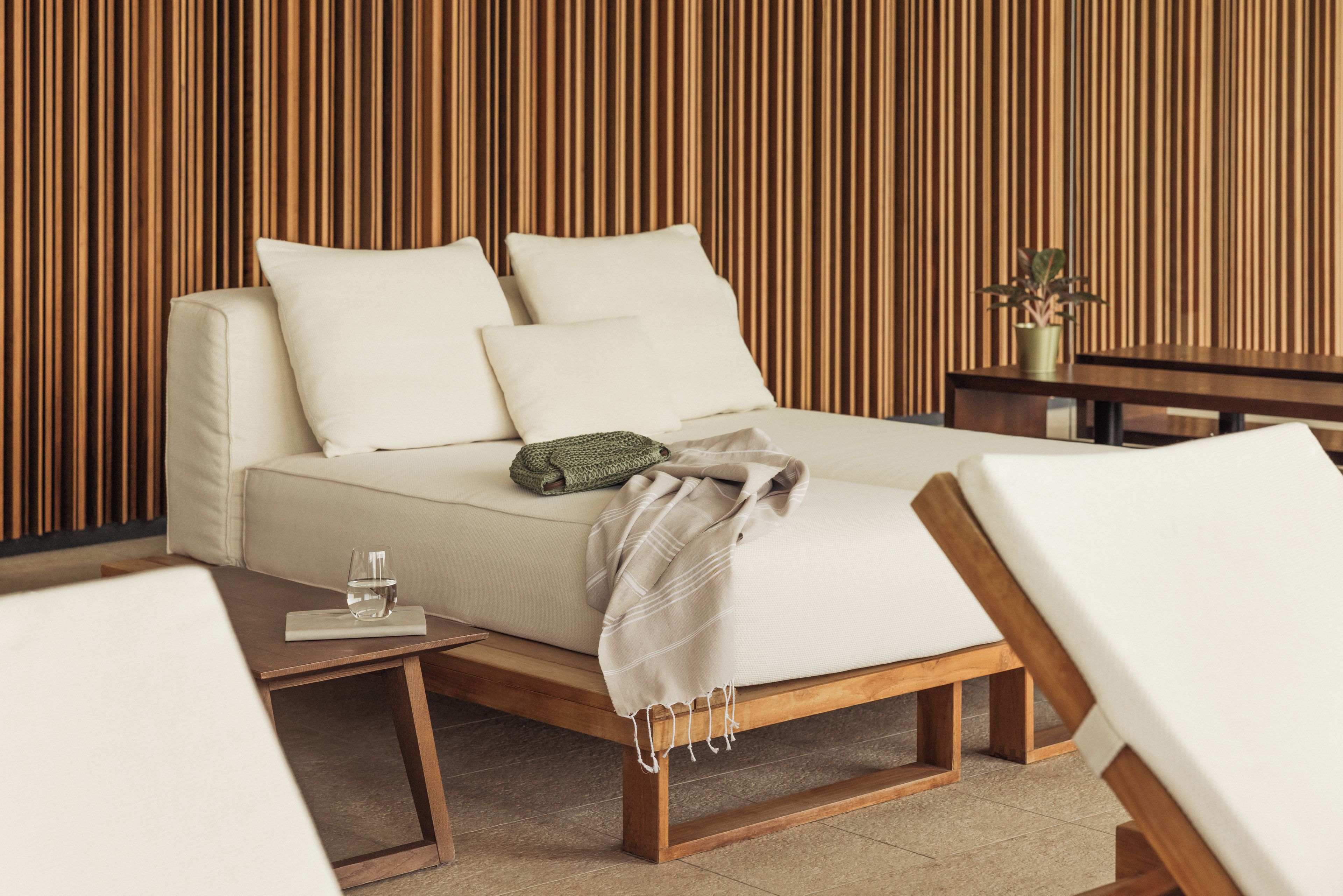 Un dormitorio moderno con sofá cama, una mesita de noche con vaso de agua y paneles de madera en la pared.