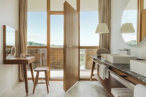 A modern bathroom with a wooden vanity, a large mirror, and a view of the outdoors through a sliding door. - Falkensteiner Balance Resort Stegersbach (Stegersbach)