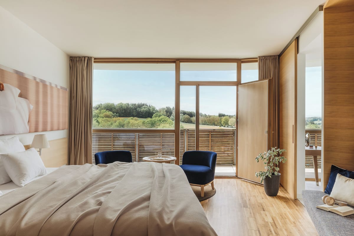 A modern hotel room with a large bed, a seating area with a table, and a view of the outdoors.