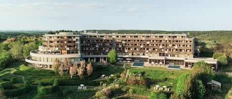 A multi-story hotel with a central courtyard, surrounded by lush greenery and hills in the background.