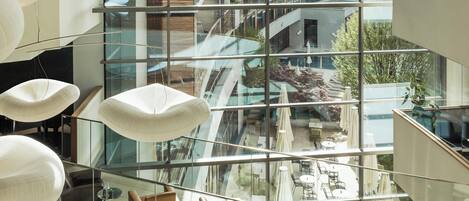 A modern interior with glass railings, contemporary furniture, and a view of a residential area through large windows.