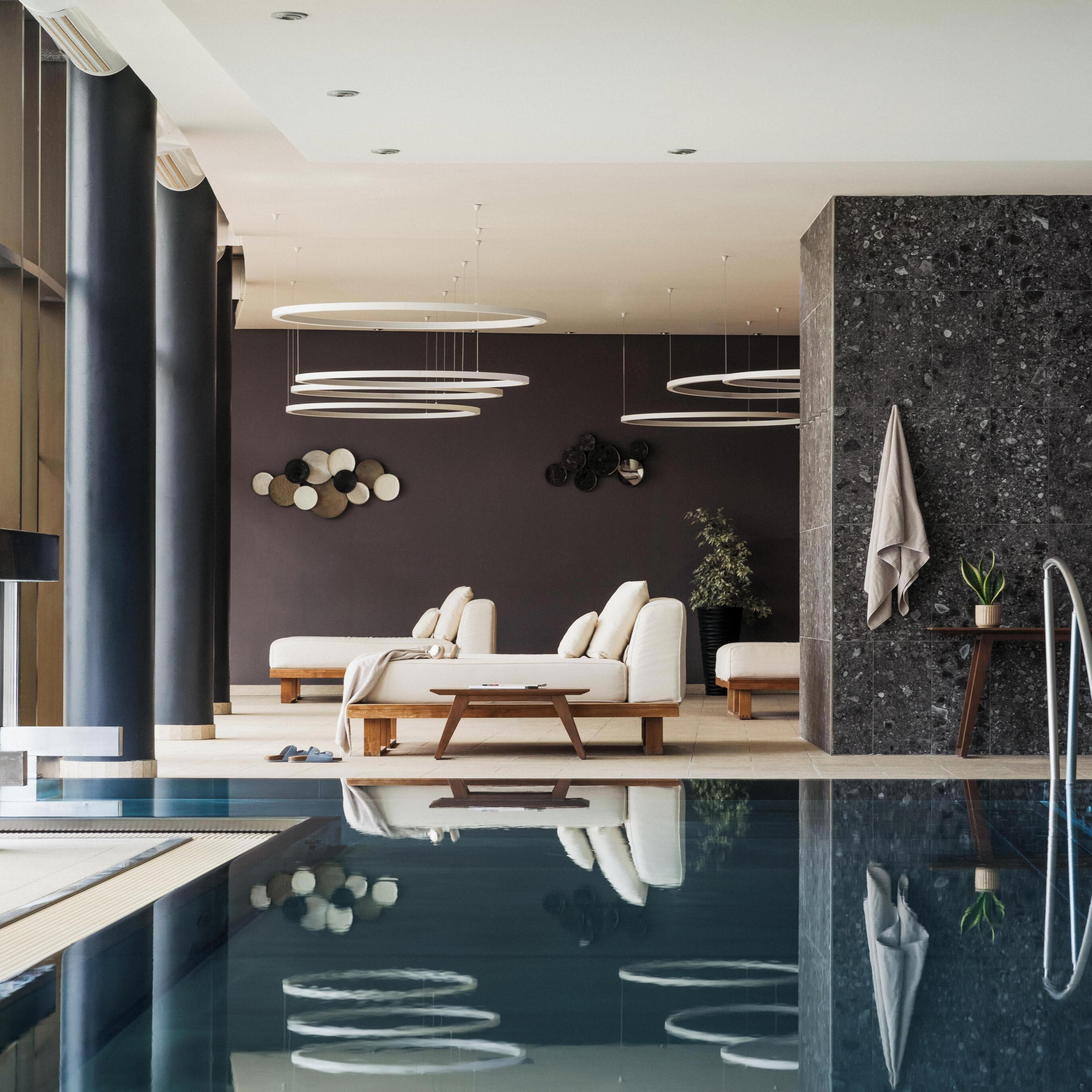 Un intérieur moderne avec une piscine, un ensemble de canapés et un mur foncé orné d’assiettes décoratives.