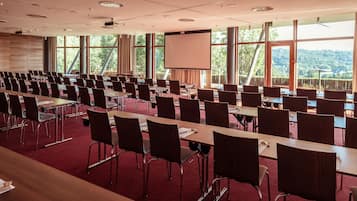 Una sala conferenze con file di tavoli e sedie, ampie finestre e uno schermo per proiezioni.