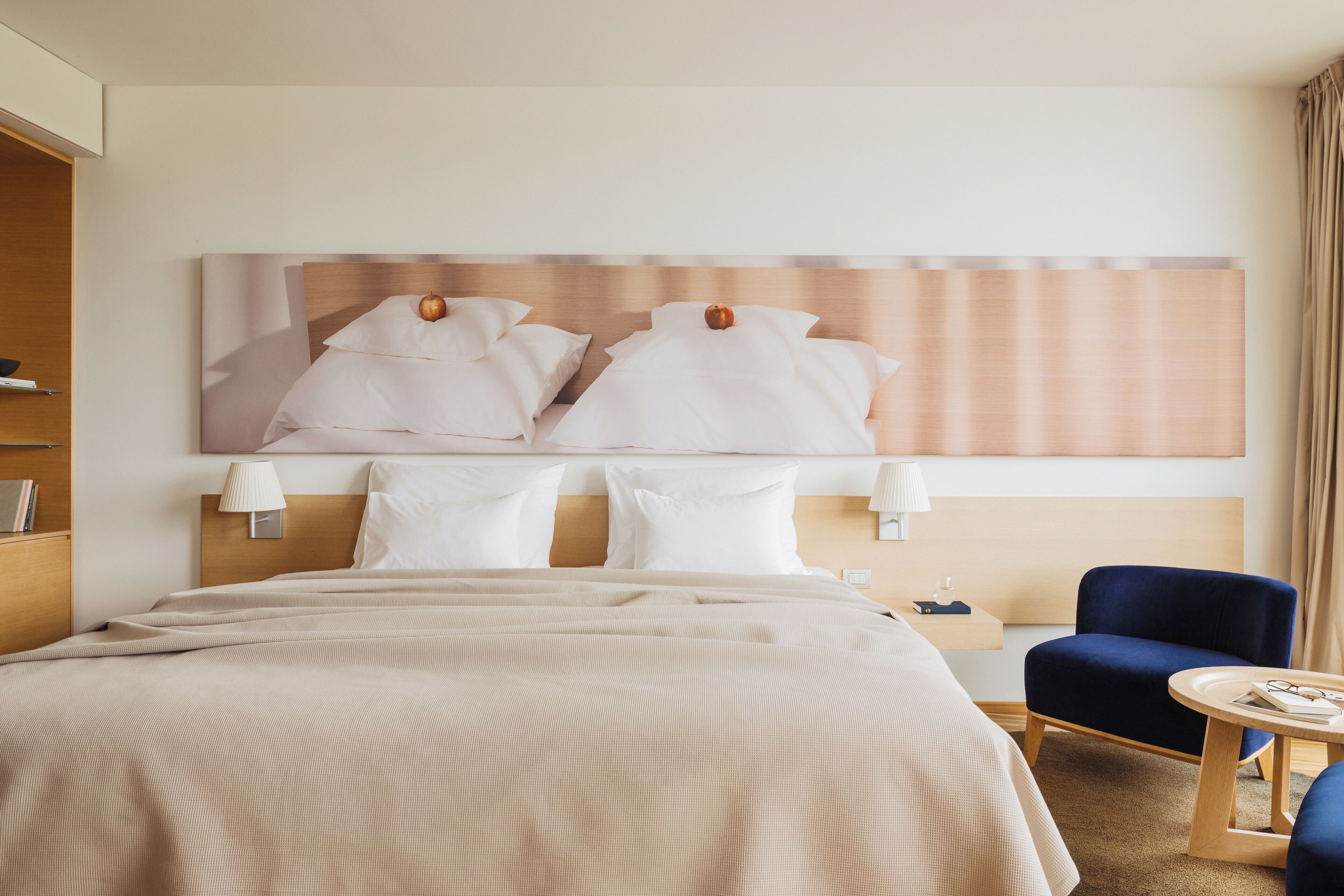 Habitación de hotel con una cama grande, dos mesitas de noche, una silla y una obra de arte colgada en la pared.