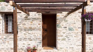 Ein Steinhaus mit einer Holztür, einer Holzpergola und einem Blumenkorb, der herunterhängt.