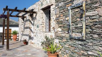A stone building with a wooden pergola, potted plants, and a window with a metal grille.