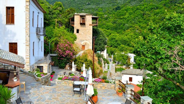 Ein gepflasterter Innenhof mit Außenbestuhlung, ein Steinturm und üppiges Grün im Hintergrund.