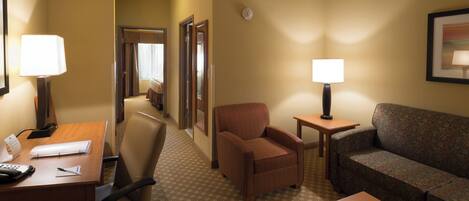A hotel room with a desk, two chairs, a sofa, a small table, and a lamp.