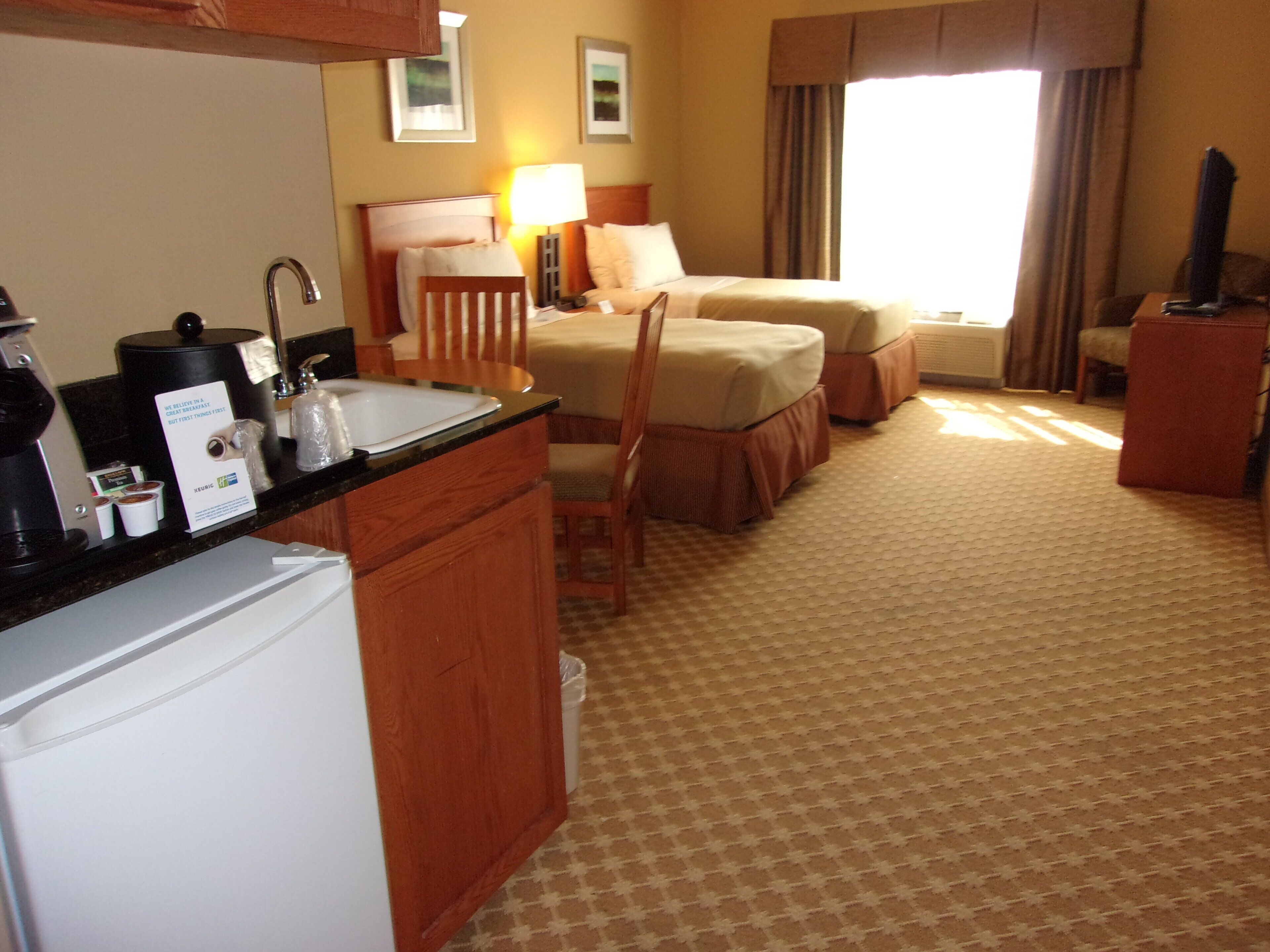 Una habitación de hotel con kitchenette, una cama, una silla, un escritorio y un televisor.