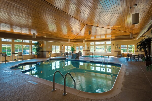 An indoor swimming pool with multiple lanes, surrounded by seating areas and windows.